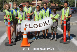 A group of people in traffic vests hold a sign that reads "Look"