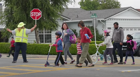 Adults and children crossing an intersection on a crosswalk. 