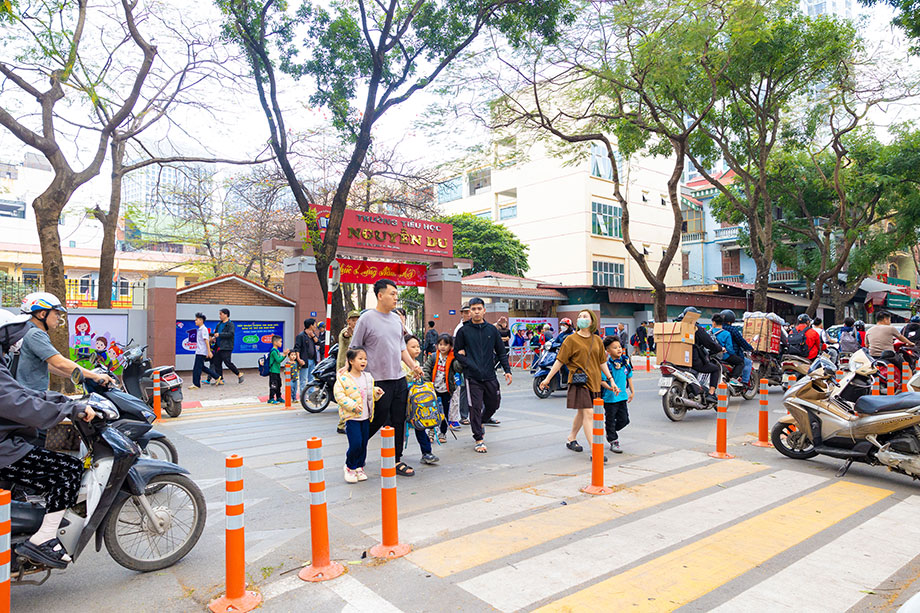 Adults and children crossing a crosswalk on a busy city street.