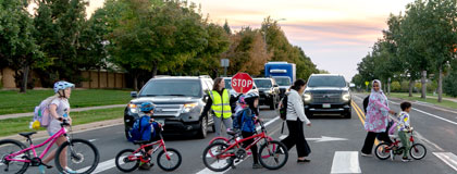 kids with bikes crossing at the crosswalk with traffic guard holding stop sign