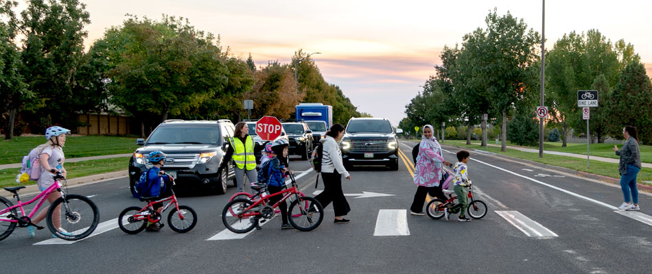 kids walking and on bikes crossing a street at the crosswalk with a guard holding a stop sign